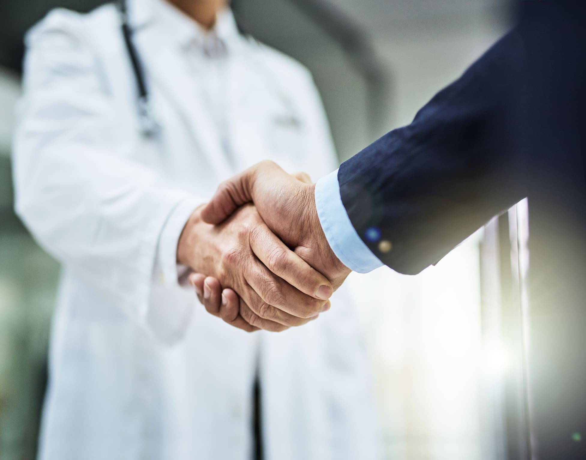 Doctor and business representative shaking hands after completing a business deal.